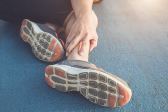 Injury from workout concept : The asian man use hands hold on his ankle while running on road in the park. Focus on ankle.