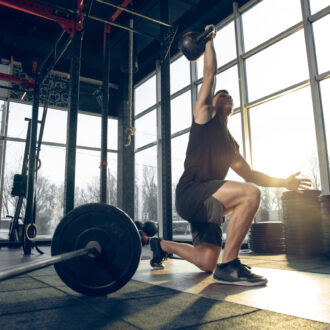 Control. Young muscular caucasian athlete training in gym, doing strength exercises, practicing, work on his upper body with weights and ball. Fitness, wellness, sport, healthy lifestyle concept.